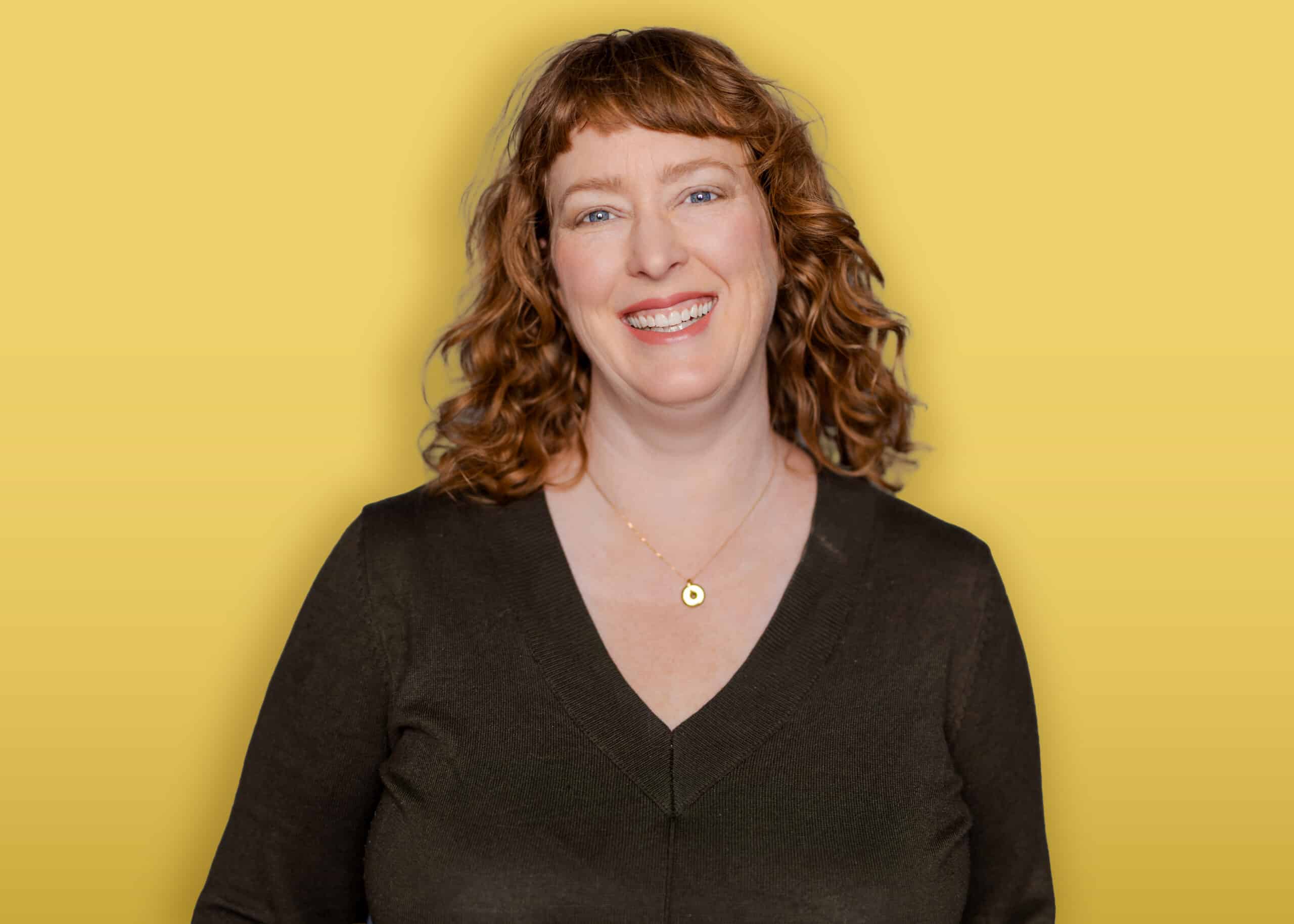 A person with dark hair, wearing a black headband, a green button-up shirt over a black top, and earrings stands in front of a yellow background and smiles at the camera.